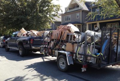 Vehicles carrying junk and hauling materials drive away from a site, clearing debris and waste.
