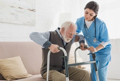 Doctor helping to retired man, getting up from sofa