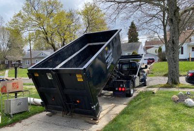 A truck hauling a dumpster filled with waste, moving away from the site for disposal.