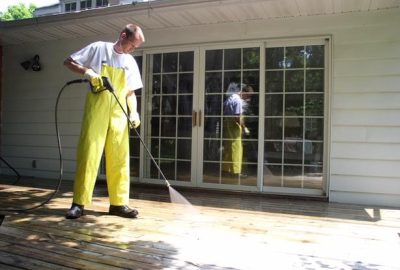 A worker cleaning the exterior floor of a house using a pressure washer to remove dirt and grime.