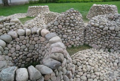 *   Image content: Several piles and low walls made of smooth, light-colored river stones/cobblestones.
    *   Setting: A gr