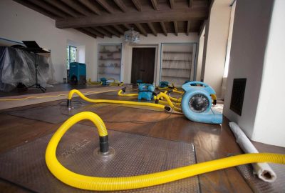 *   Image content: A room with wooden floors and a beamed ceiling.
    *   Key elements: Multiple blue air movers/blowers, ye
