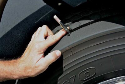 Hand using a tread depth gauge to measure the wear on a car tire.