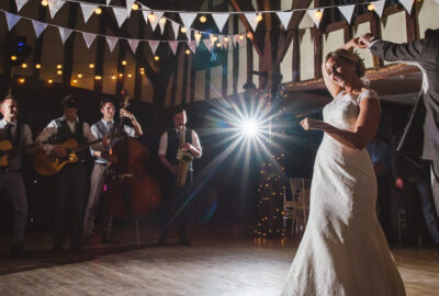 A bride and groom dance in a rustic barn during their wedding reception, accompanied by a live band.