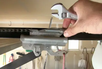 Hand holding an adjustable wrench to adjust a bolt on a garage door opener trolley.
