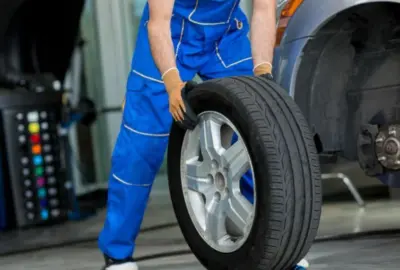 Mechanic in blue overalls holding a car tire in an auto repair shop.