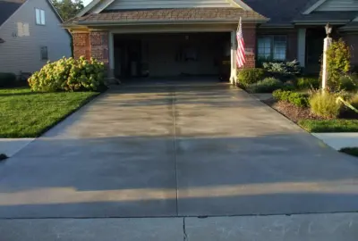 A concrete driveway leads to an open garage of a single-story house with an American flag.