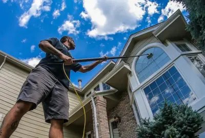 Man using a telescopic pole to clean a high arched window on a house.