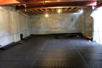 Basement under construction with white waterproof membrane on the walls and black dimpled membrane on the floor.