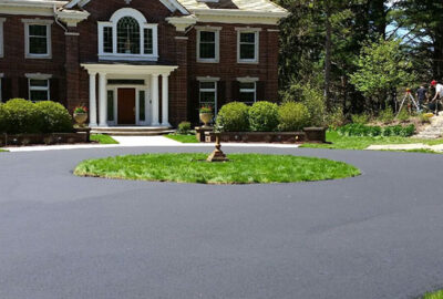 Large brick mansion with a freshly paved circular asphalt driveway and a center grassy island.