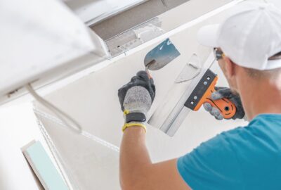 Worker applying plaster to drywall seams using a putty knife and spreader.