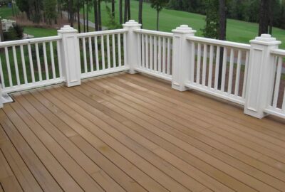 Brown composite deck with white railings and decorative posts overlooking a wooded lawn.