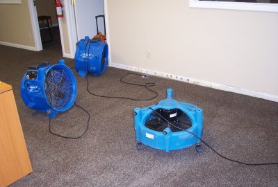 Three blue industrial air movers positioned on a grey carpeted floor.