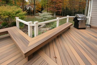 *   Image content: A wooden deck with a built-in L-shaped bench, a white railing with cable infill, a stainless steel gas gri