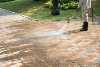 Person using a pressure washer to clean a patterned stone pavement walkway.