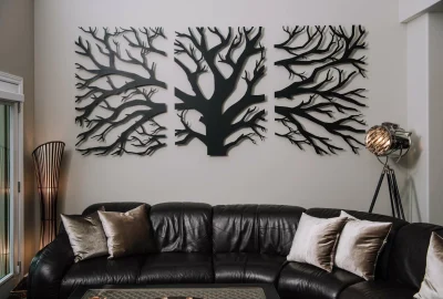 Triptych of black metal tree branch art hung above a dark leather sectional sofa in a modern living room.