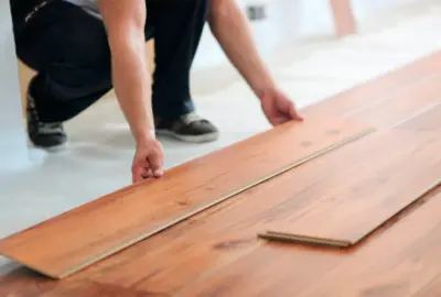 Person installing light brown wood-grain laminate flooring planks.