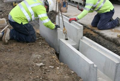Construction workers in high-visibility gear installing precast concrete blocks in a trench.