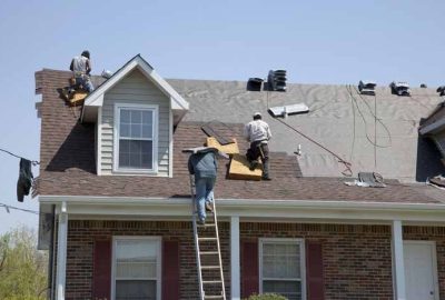 *   Image shows three workers on a house roof.
    *   One worker is on a ladder climbing up.
    *   One worker is on the pe