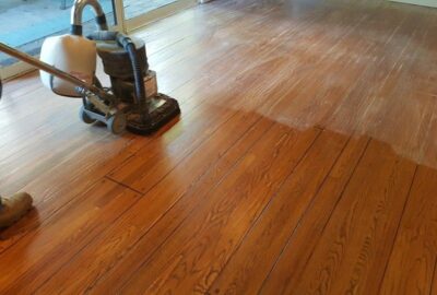 A professional floor polisher restoring a hardwood floor, showing the contrast between dull and glossy wood.