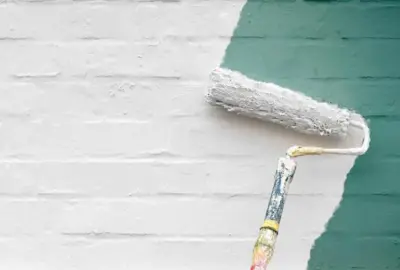 Paint roller applying white paint over a teal brick wall.