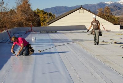 Roofers installing a white flat roof membrane with mountains in the distance.