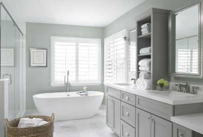 Bright modern bathroom with a white freestanding tub, grey double vanity, marble floors, and light green walls.