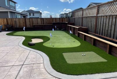Backyard putting green with artificial turf, white flags, a sand trap, and a tee area.