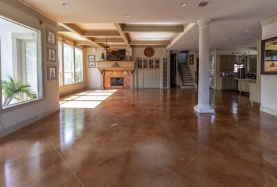 Spacious open concept living area with polished brown concrete floors, a large fireplace, and a white classical column.