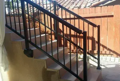 Concrete outdoor stairs with black metal railings and a brown wooden fence in the background.
