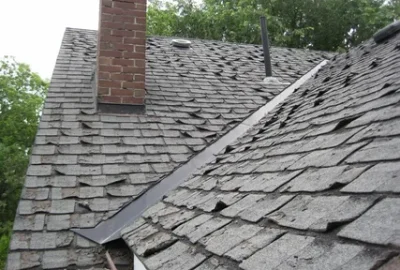 Roof with worn, curling gray asphalt shingles and a brick chimney.