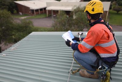 Rope access inspector technician holding looking at the paper work while inspecting fall arrest, fall restraint roof anchor point horizontal safety line Sydney, CBD, Australia