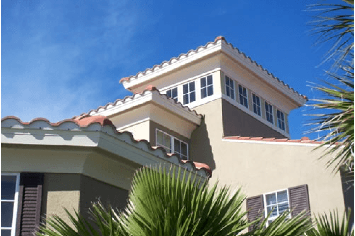 *   Image: A low-angle shot of a Mediterranean-style house with tan stucco walls, red tile roofs, and multiple windows. There