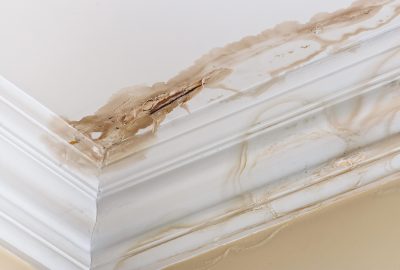 Peeling paint on an interior ceiling a result of water damage caused by a leaking pipe dripping down from upstairs.