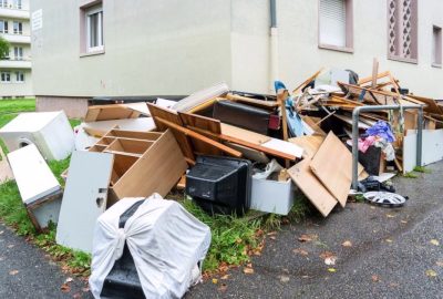 Large pile of discarded furniture and household items on a sidewalk next to an apartment building.
