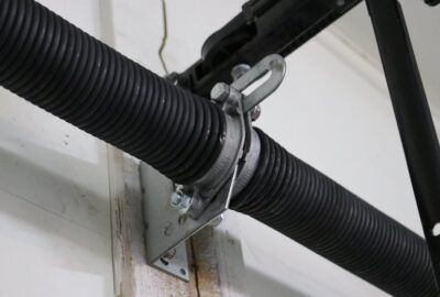 Close-up of a metal bracket securing a black corrugated hose to a wall.