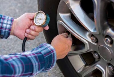 A person checking a car tire's air pressure with a handheld dial gauge.