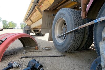 Person using a torque wrench to tighten lug nuts on a yellow dump truck's wheel.