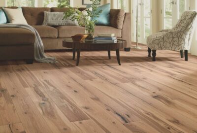 Rustic wide-plank hardwood floors in a living room with a brown sofa and patterned accent chair.
