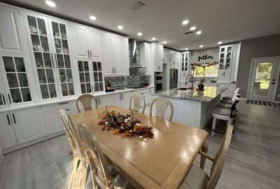 Modern white kitchen with a marble island and a wooden dining table decorated with an autumn centerpiece.