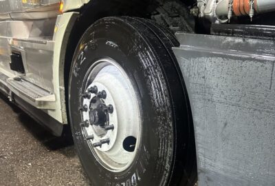 Close-up of a wet semi-truck wheel and exposed engine components.