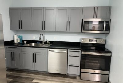 Modern kitchen with gray cabinets, black countertops, and stainless steel appliances.
