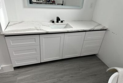 White bathroom vanity with a white marbled quartz countertop, black faucet, and gray tile flooring.