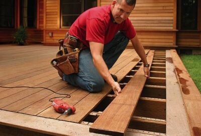 Man in a red shirt and tool belt installing wooden planks on a deck.