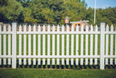 White picket fence in a green grassy yard with blurred trees in the background.