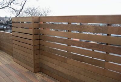 Modern brown horizontal slat wooden privacy fence on a wooden rooftop deck.