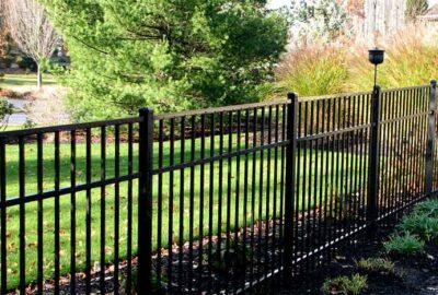 Black metal fence bordering a green lawn and landscaped garden bed.