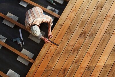 Top-down view of a carpenter measuring light brown wooden deck planks during construction.