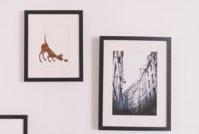 Two framed prints hanging on a white wall: one shows a brown dog with a hedgehog, the other a black-and-white city street.