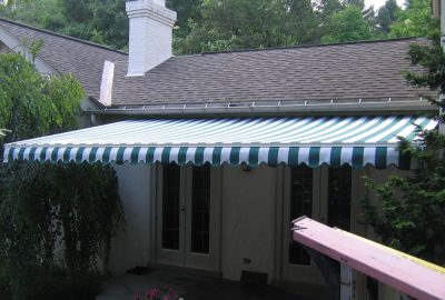 Green and white striped retractable awning mounted over French doors on a house patio.